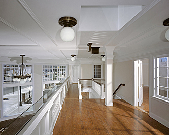 Upstairs interior of a former auto showroom showing hardwood flooring, white painted woodwork, detailed celing with white globe chandeliers, and a view down to the mezzanine