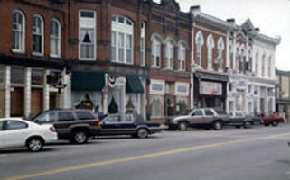 rowhouses along a street with shops on the ground floor and cars parked at angles in front of them