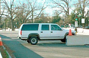 Concrete jersey barriers line a road and partially block it aling with a Chevy Suburban