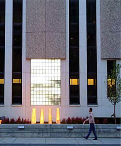 man walking along a sidewalk in front of a building's security wall featuring a public artwork